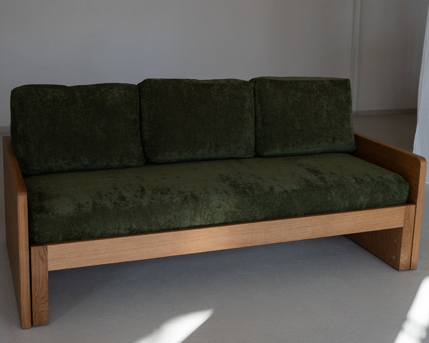 Green sofa with wooden frame against a plain wall