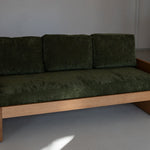 Green sofa with wooden frame against a plain wall