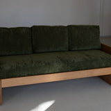 Green sofa with wooden frame against a plain wall