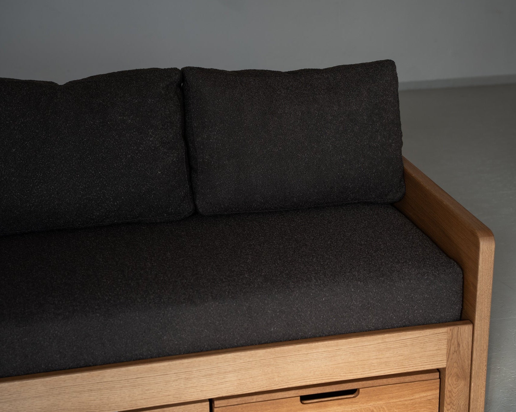 Dark gray cushioned sofa with wooden frame against a plain wall.