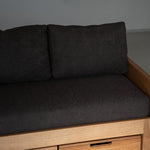 Dark gray cushioned sofa with wooden frame against a plain wall.