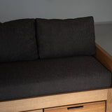 Dark gray cushioned sofa with wooden frame against a plain wall.