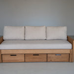 Wooden sofa bed with beige cushions against a plain wall.