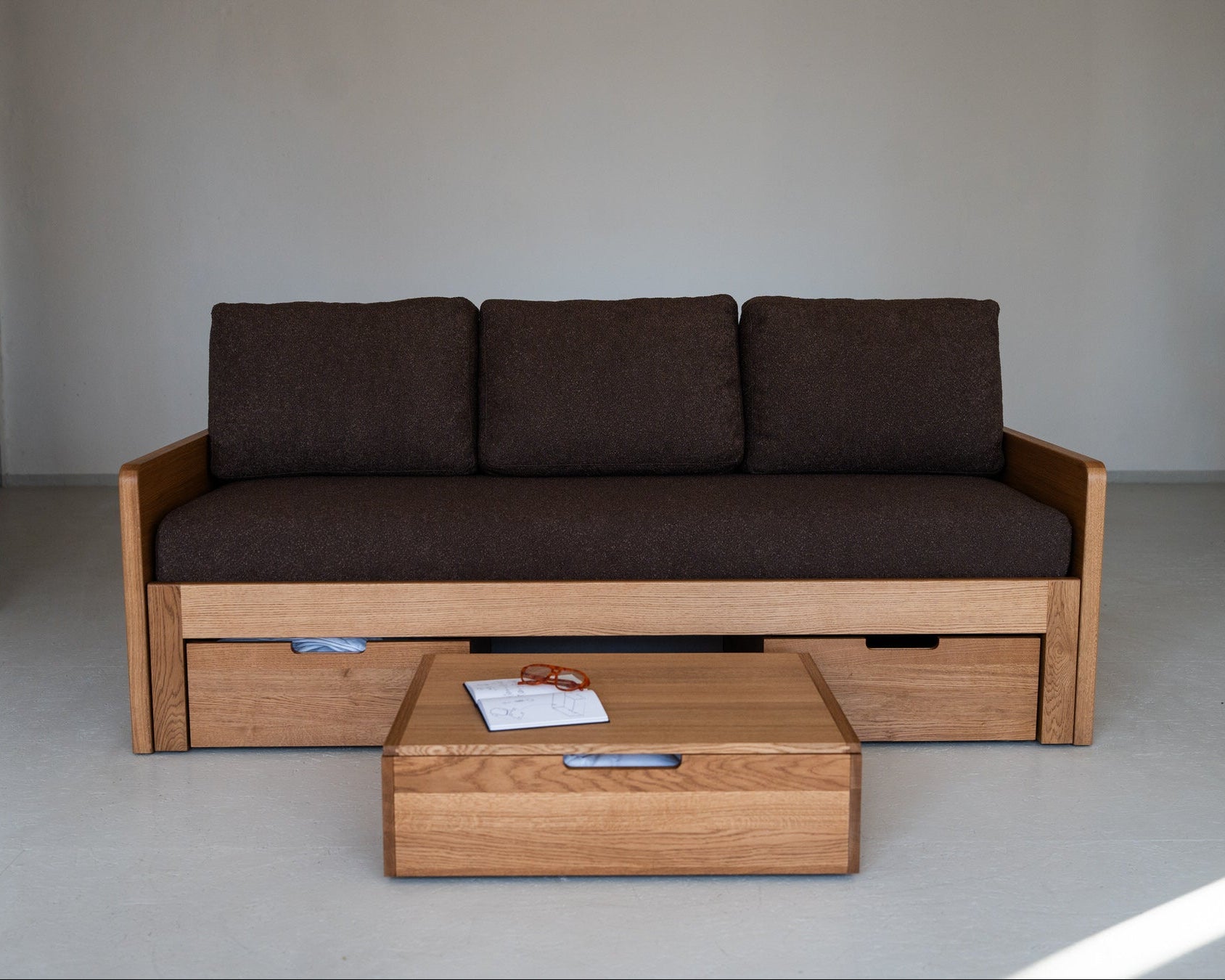 Wooden sofa with storage drawers and a matching coffee table in a minimalistic setting.