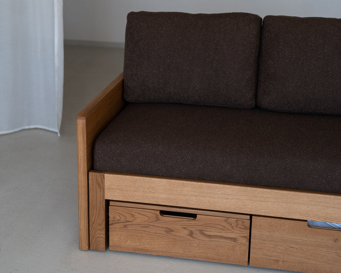 Brown sofa with wooden frame and drawers against a plain wall.