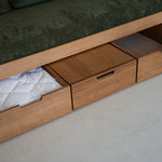 Wooden bed with storage drawers and green cushioned top.