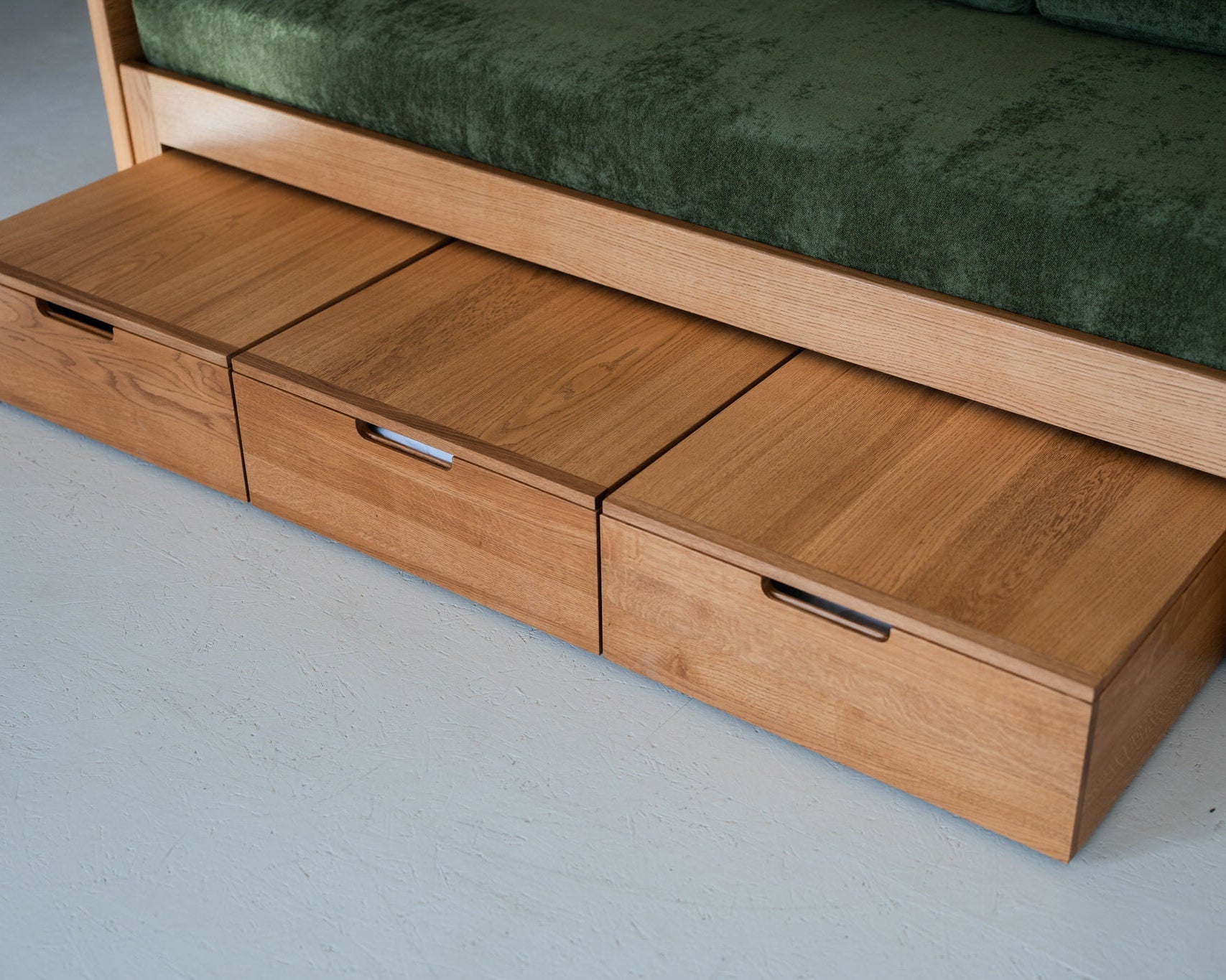 Wooden sofa bed with storage drawers on a gray floor.