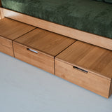 Wooden sofa bed with storage drawers on a gray floor.